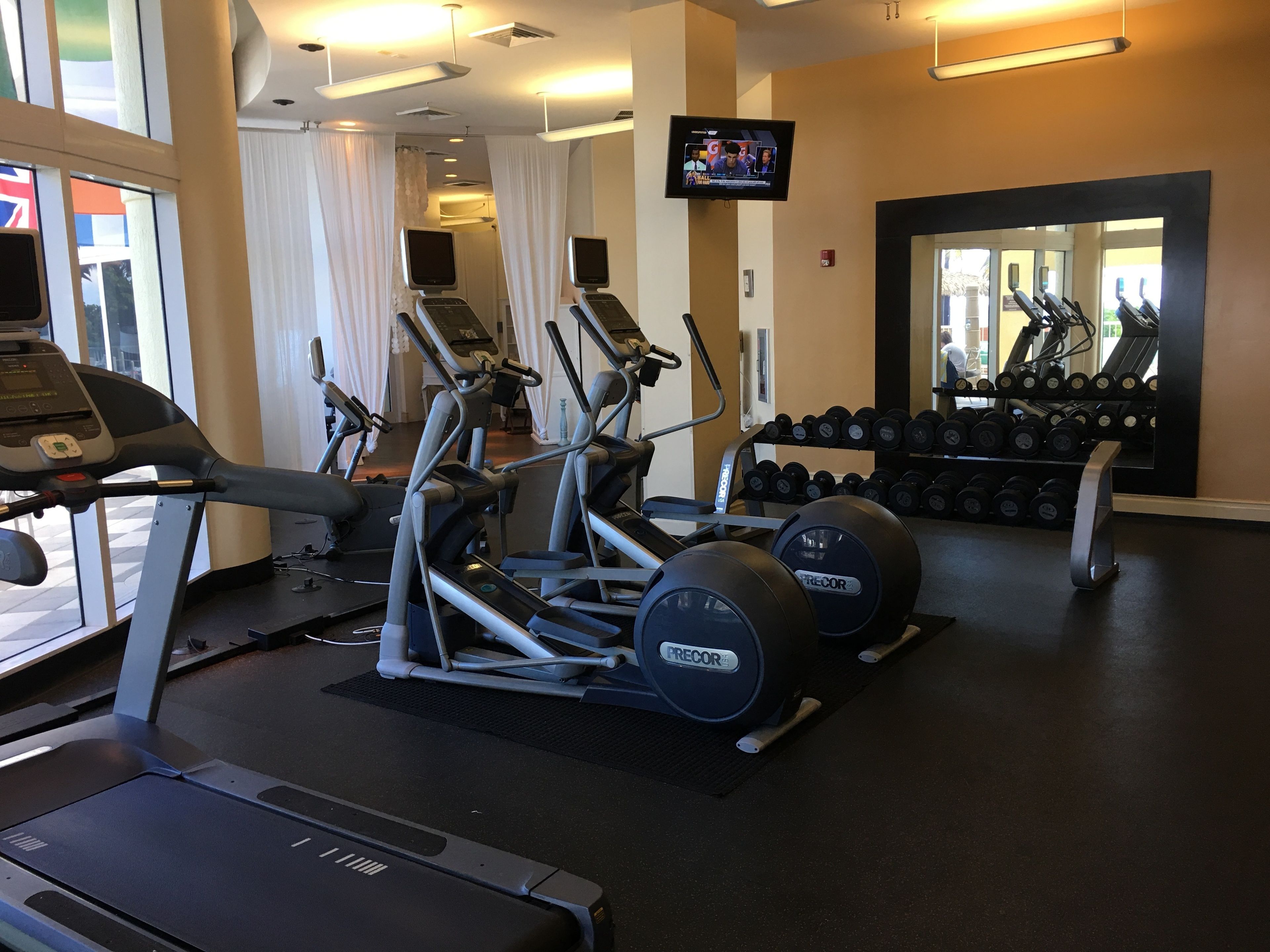 A gym with treadmills, elliptical machines, and a rack of dumbbells.
