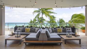 A modern outdoor seating area with a view of the ocean and palm trees.