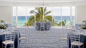 A room with round tables, clear chairs, and a view of the ocean.