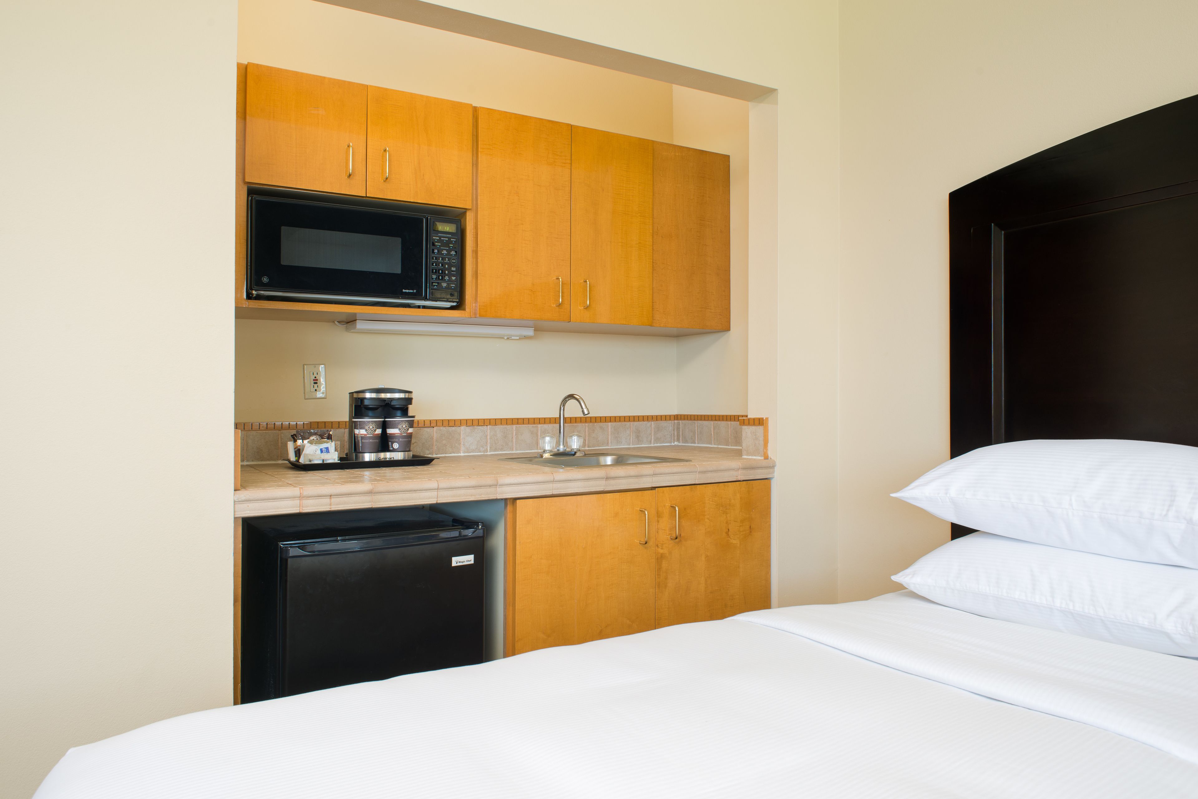 A compact hotel room with a kitchenette including a microwave, coffee maker, and sink.