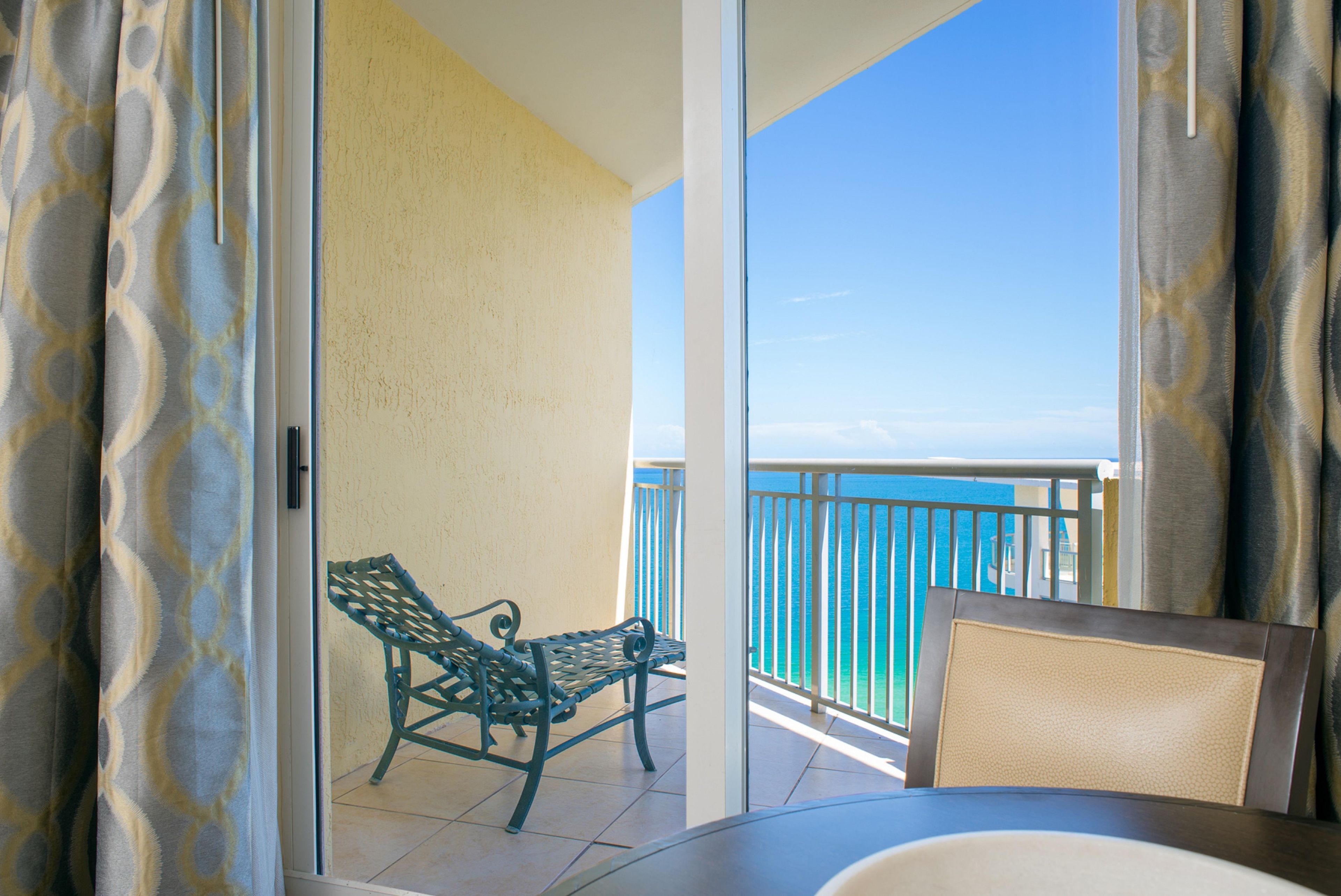 A balcony with a view of the ocean, a chair, and a table.