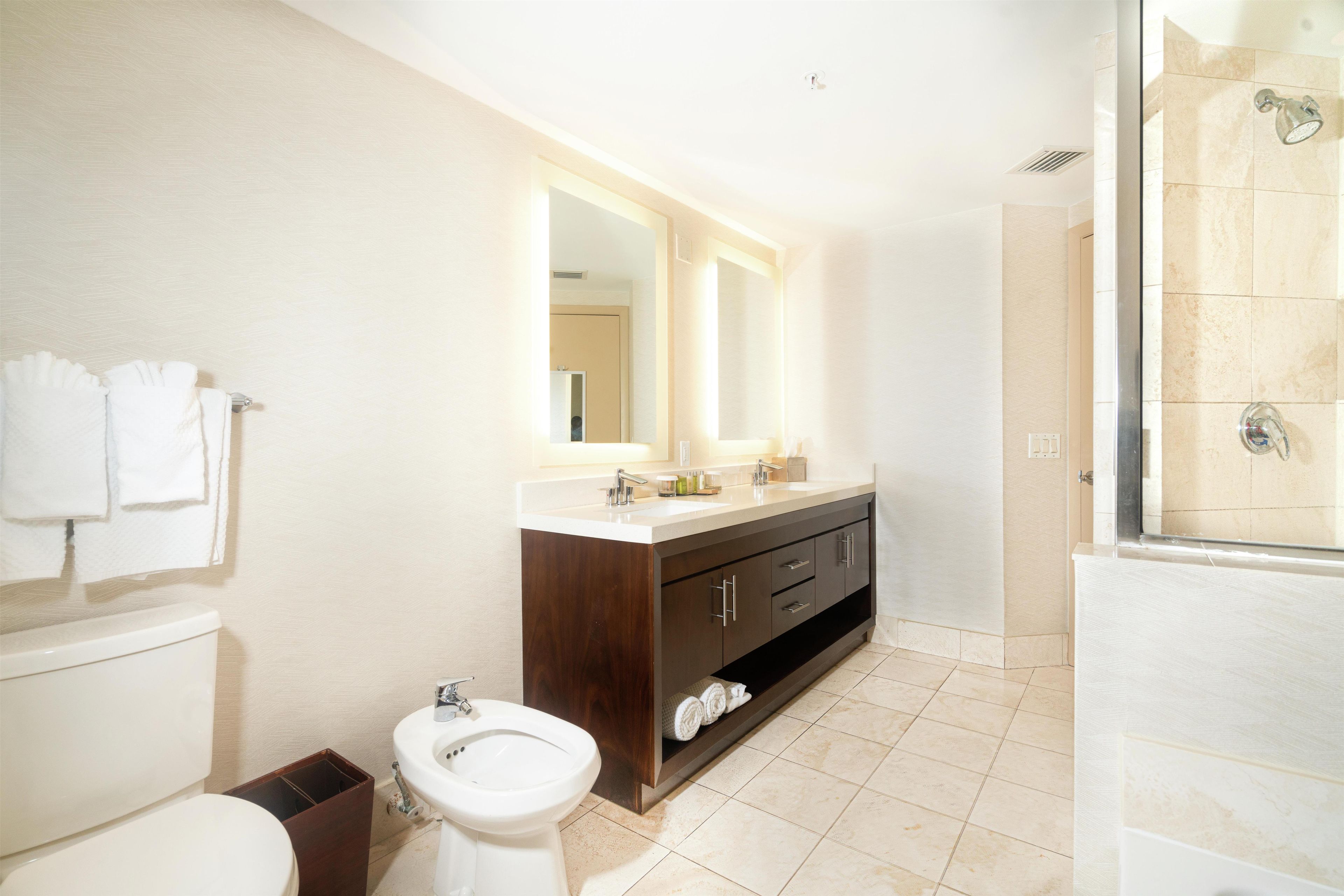 A bathroom with a toilet, bidet, sink, vanity, and a shower area.