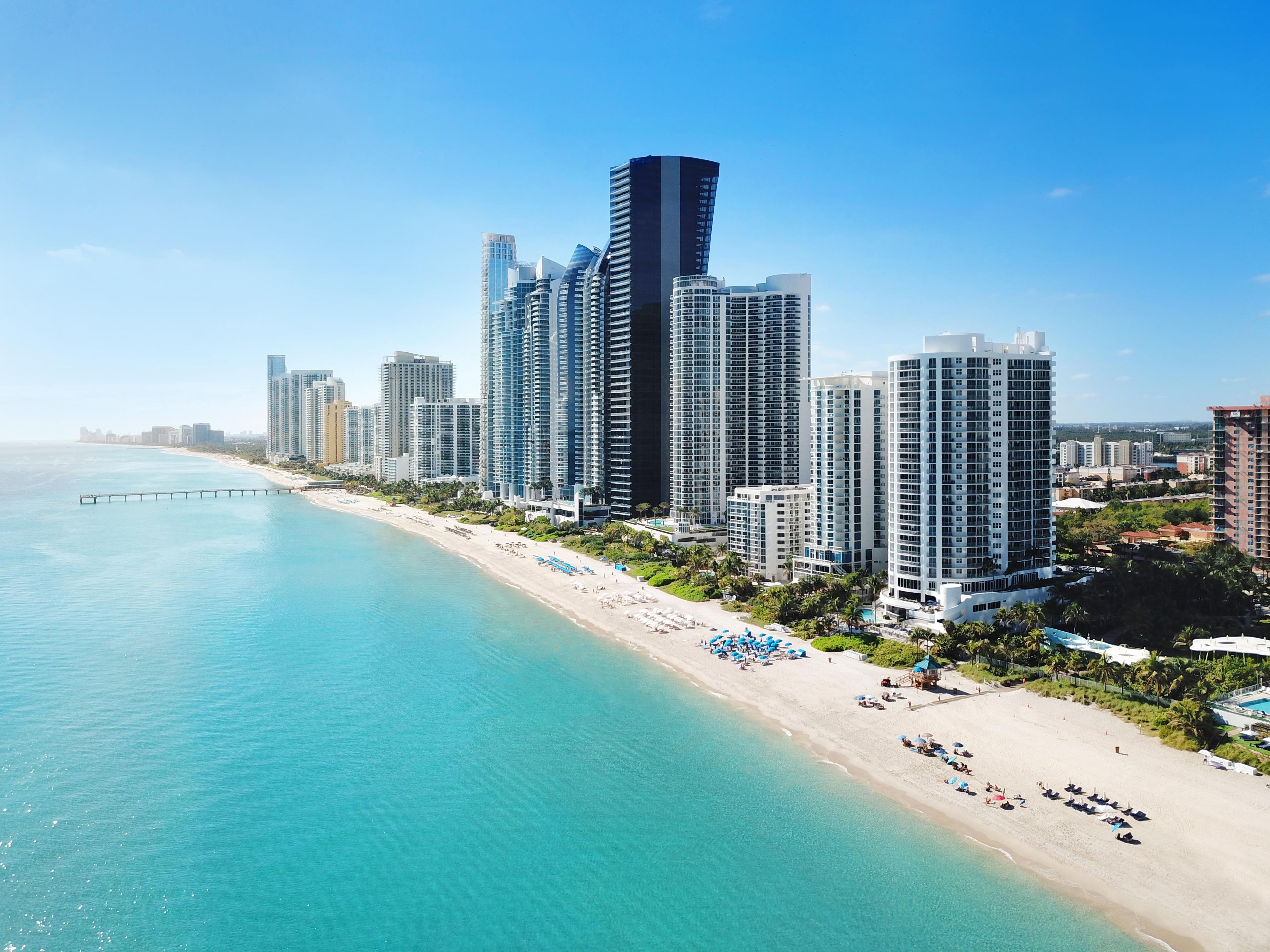 A coastal cityscape with high-rise buildings, a beach, and clear blue waters.