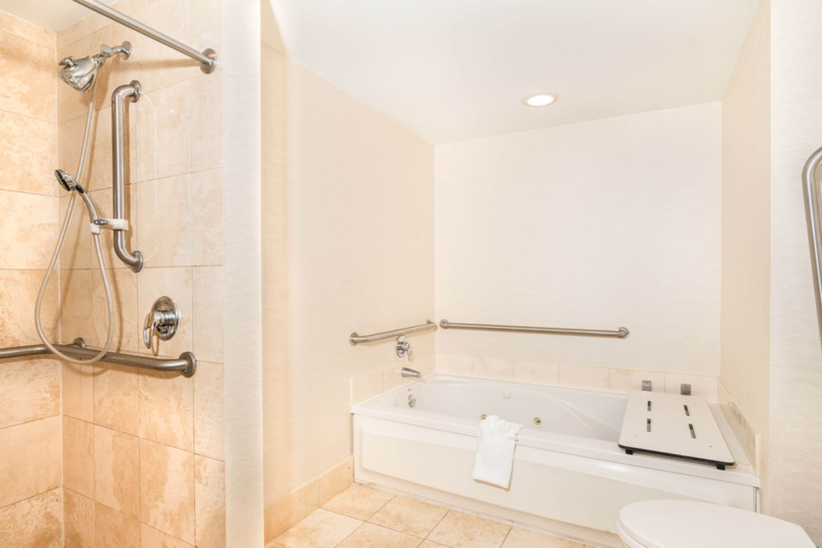 Une salle de bain équipée d’une douche, de barres d’appui, d’une baignoire et de toilettes.