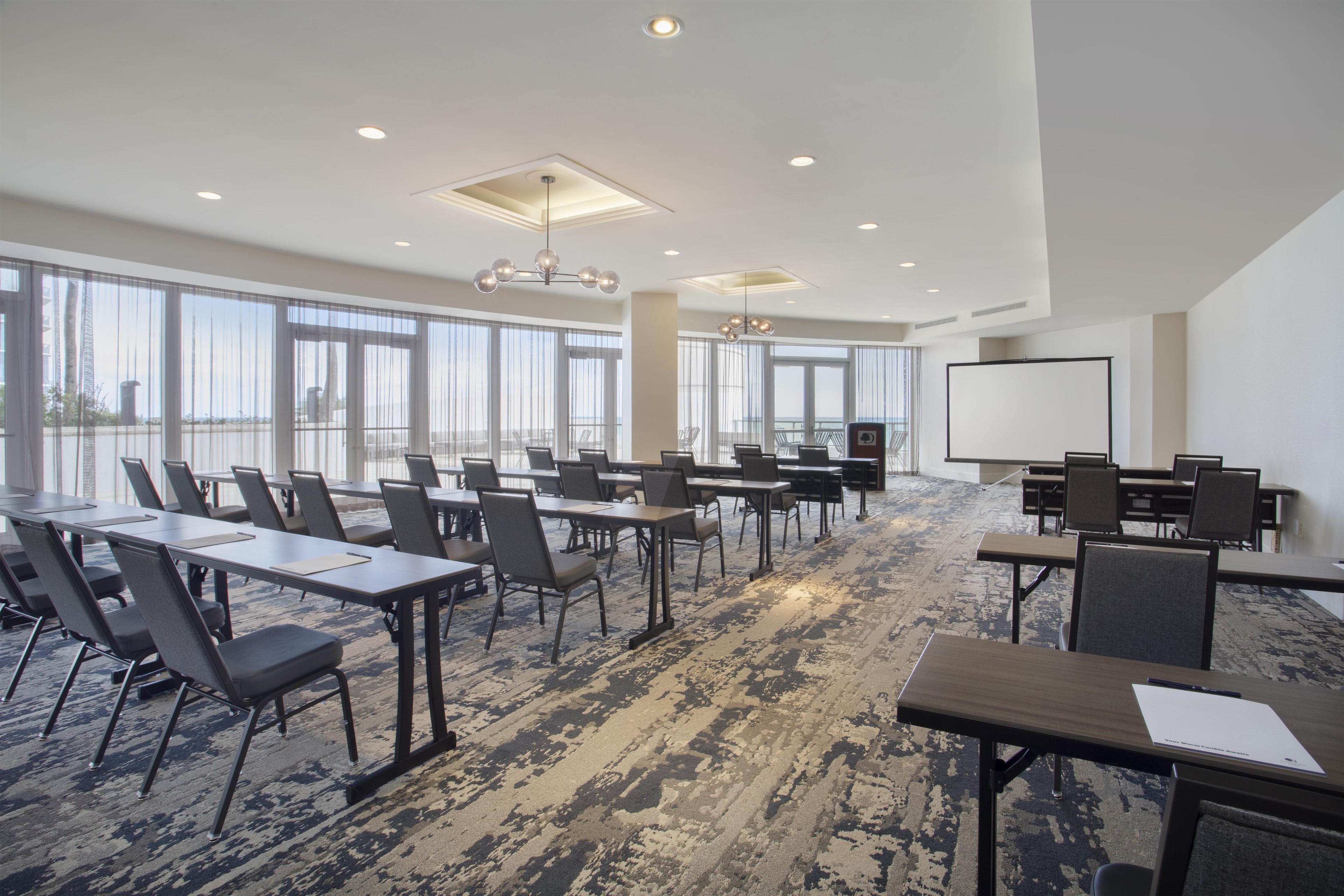 Une salle de conférence équipée de tables et de chaises, de grandes fenêtres et d’un tableau blanc.