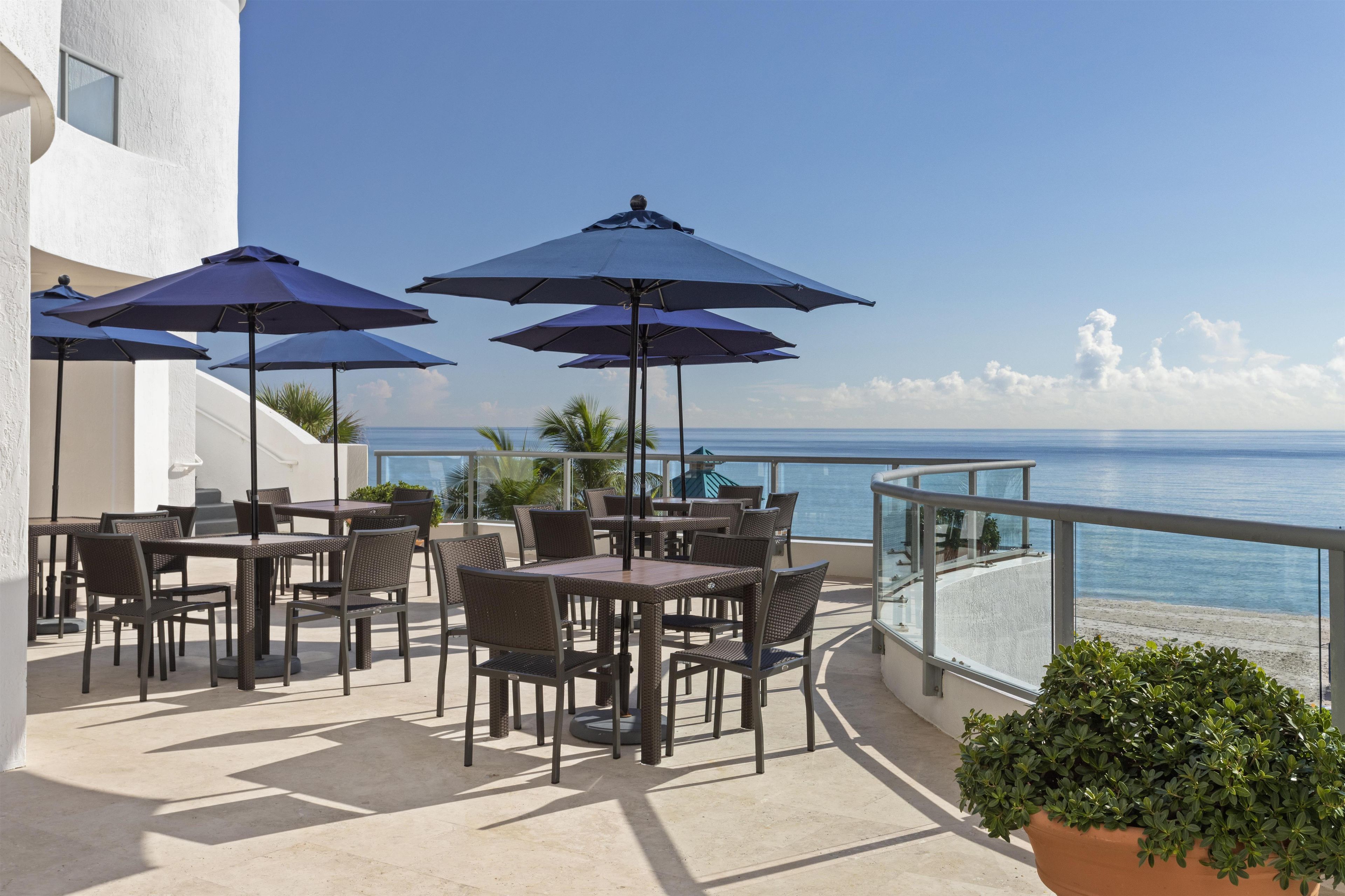 Un patio exterior con mesas y sillas, sombrillas y vistas al mar.