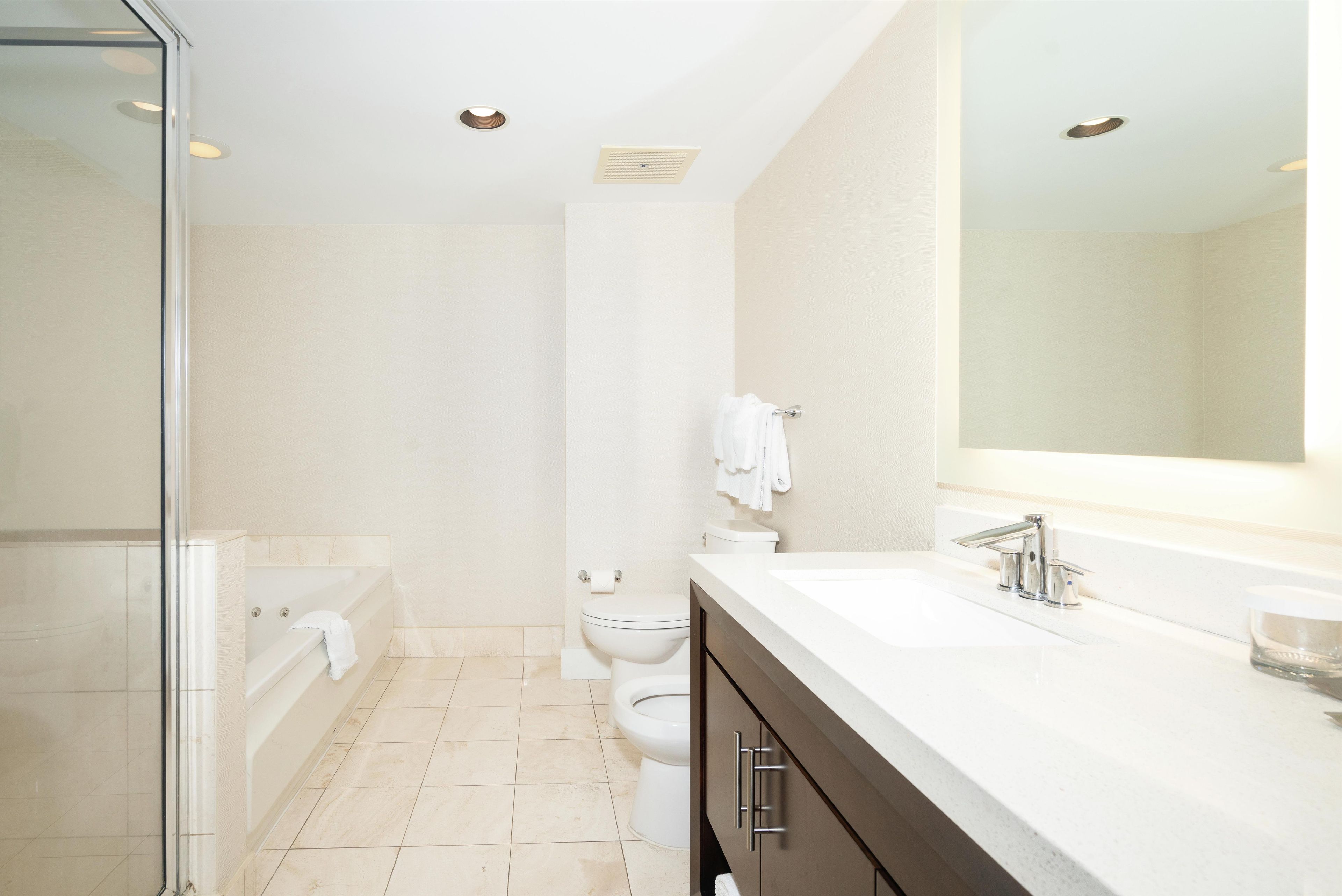 A modern bathroom with a glass shower enclosure, a bathtub, a toilet, and a vanity with a mirror.