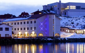 Un edificio frente al agua con varias ventanas e instalación de luces con forma de X en la fachada.