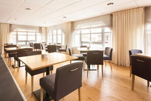 Un vaste espace dédié à la salle à manger, avec de nombreuses tables et chaises, de grandes fenêtres dotées de rideaux et un plancher en bois.
