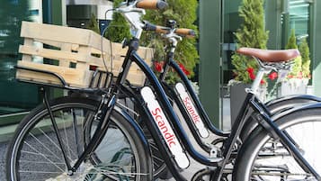 Una bicicleta con una cesta de madera en la parte delantera, estacionada frente a un edificio con puertas de vidrio y plantas en macetas.