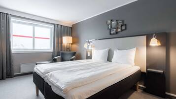 A hotel room with a large bed, a chair, a desk, and a window with curtains.