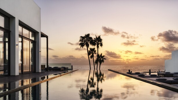 Une piscine à débordement moderne offrant une vue imprenable sur le coucher de soleil et les palmiers.