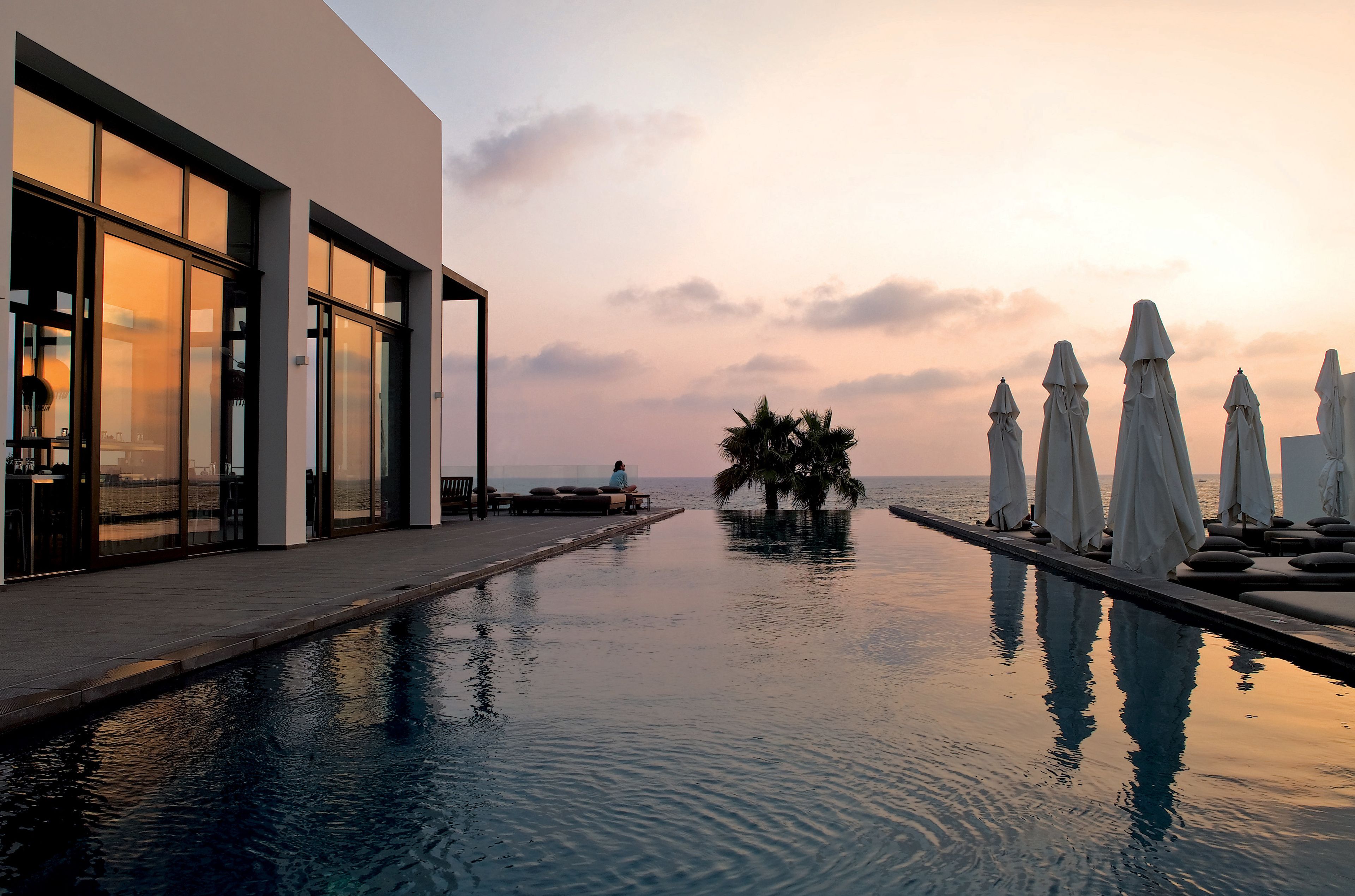A modern hotel with a pool, lounge chairs, and umbrellas.