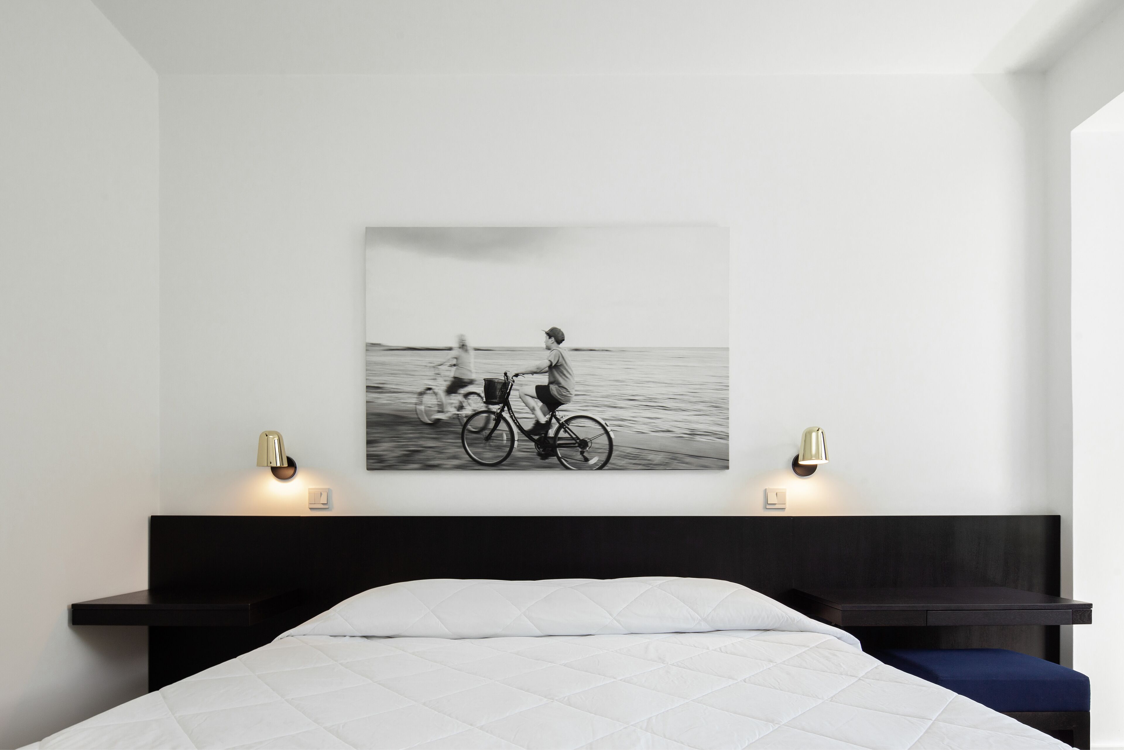 Un dormitorio con cama, cabecera, mesitas de noche y lámparas de pared.