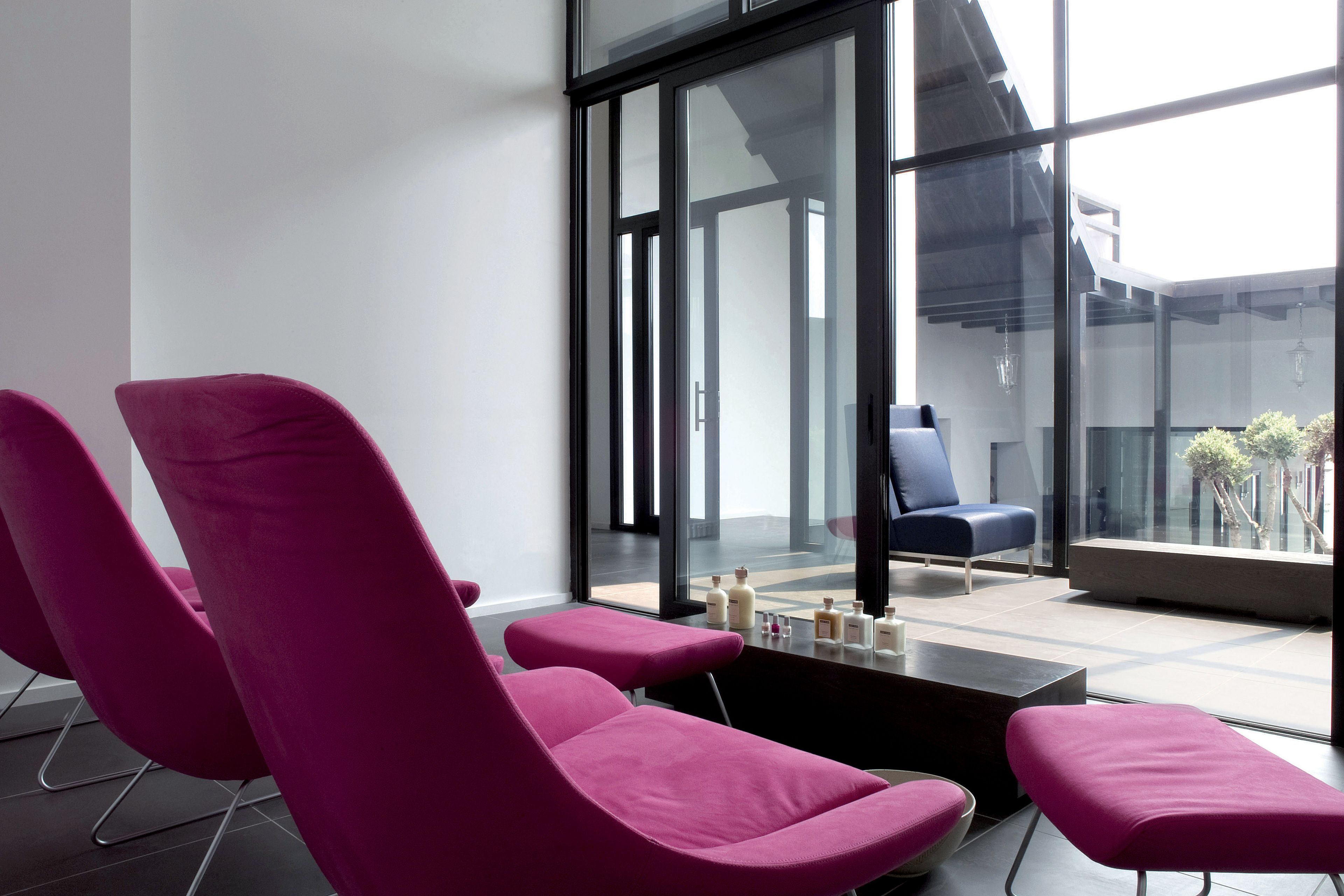 Un intérieur moderne avec des chaises roses, une chaise bleue et un mur de verre donnant sur l’extérieur.