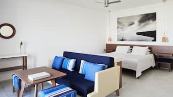 A modern hotel room with a sofa, a small table, a bed, and a nightstand.