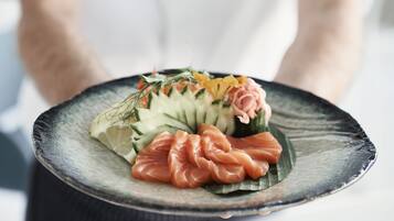 Un plato con diversos alimentos, como salmón y verduras, sostenido por una persona.