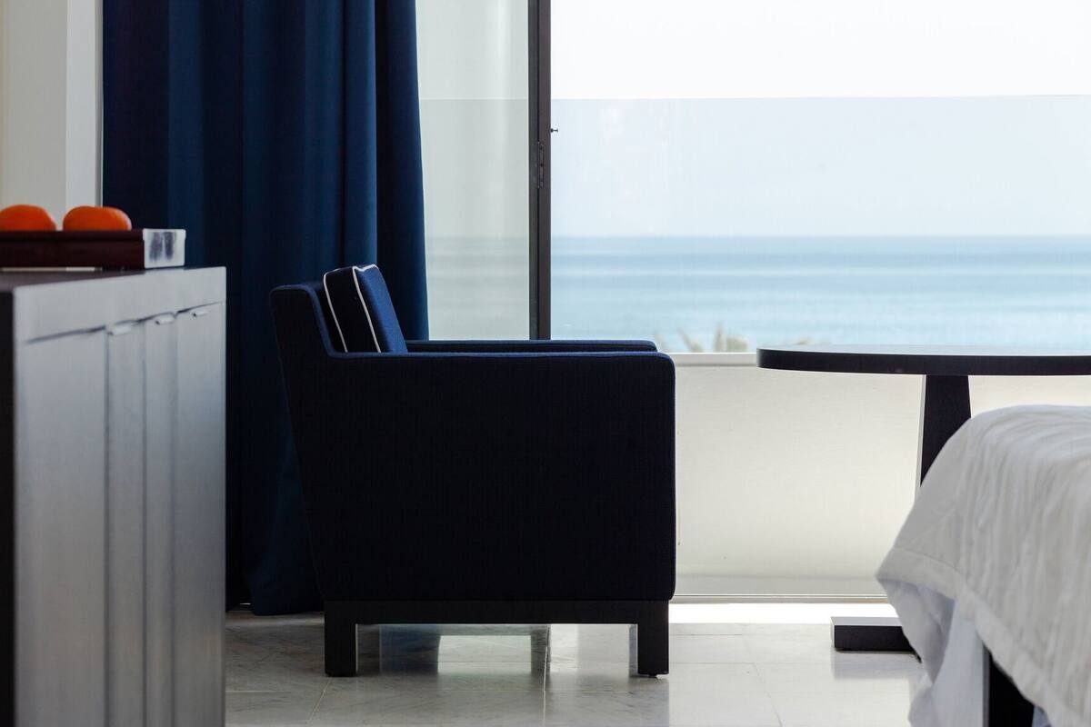 A hotel room with a view of the sea, a bed, a desk, and a chair.