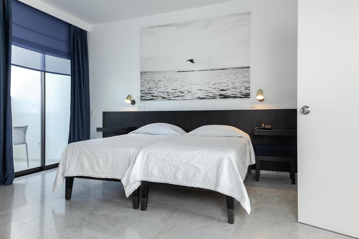 A hotel room with a bed, a desk, and a large window with curtains.