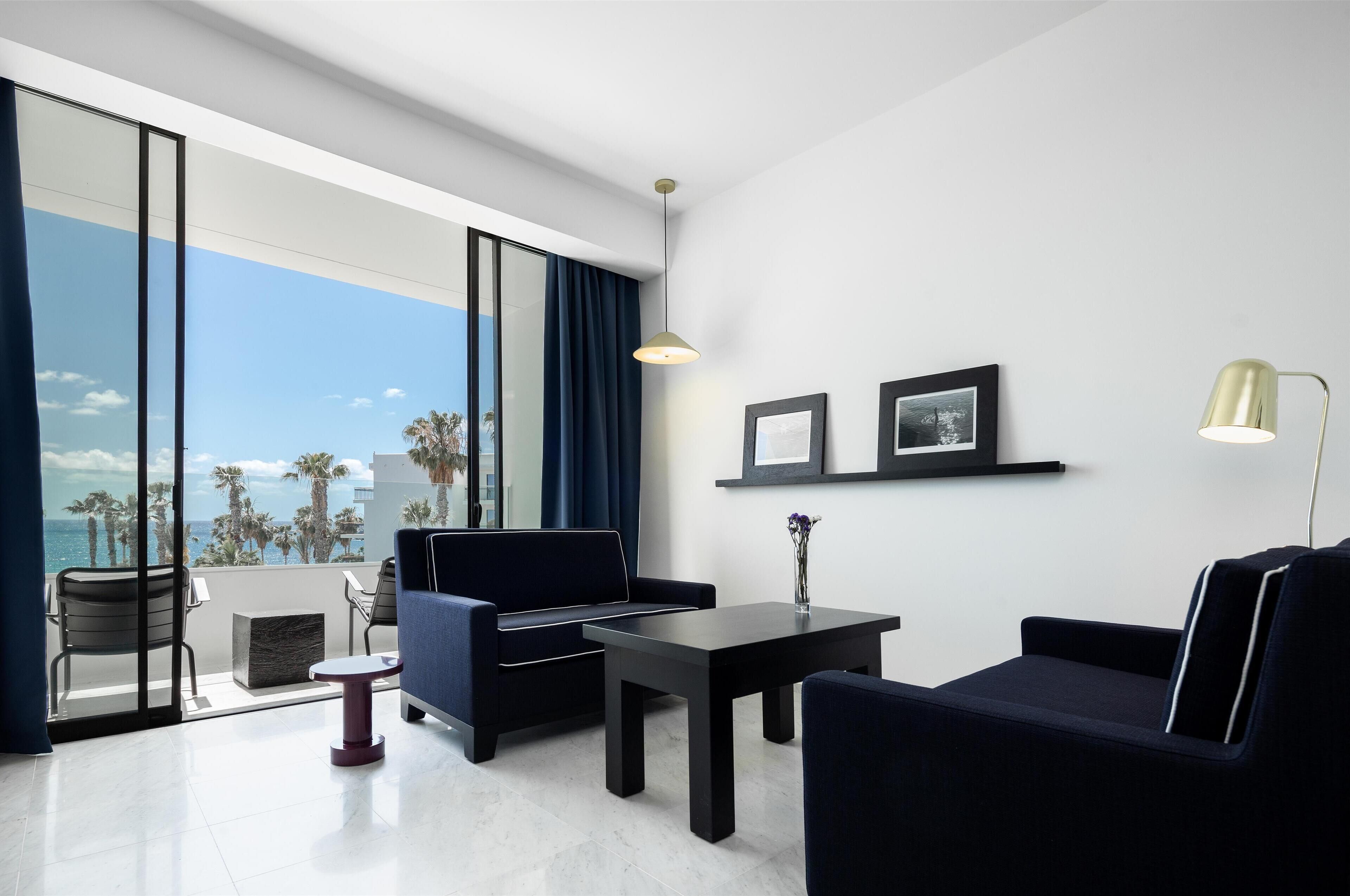 A modern hotel room with a large balcony, a sofa, a table, and a lamp.