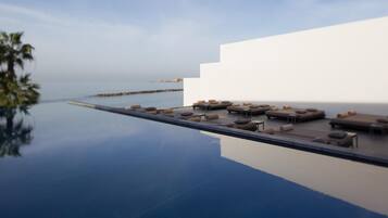 Una piscina infinita moderna con asientos exteriores y vista al mar.