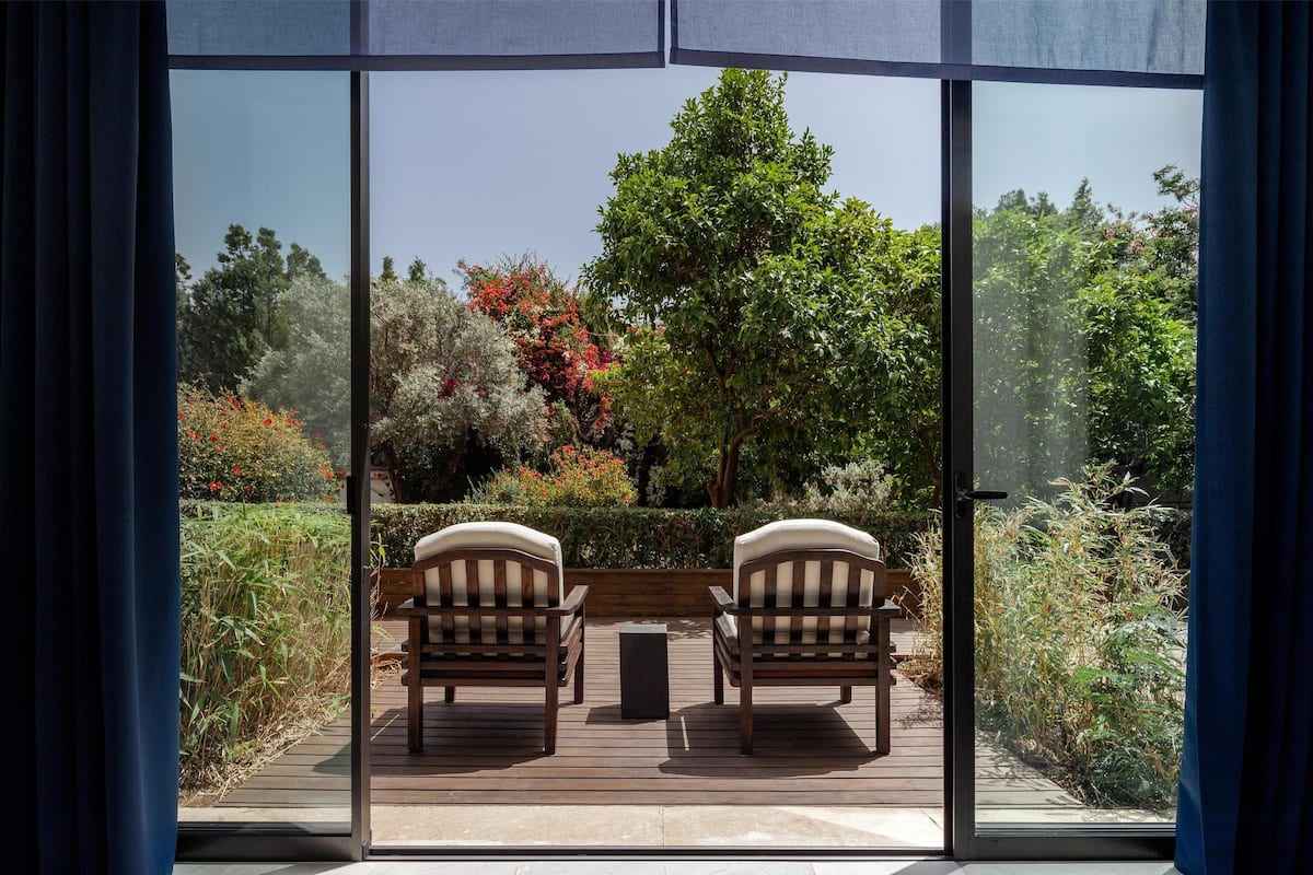 A deck with two chairs and a small table, overlooking a garden with various plants and trees.