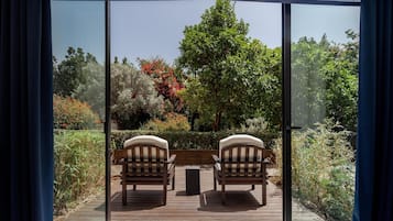 Una terraza con dos sillas y una mesita, con vistas a un jardín con diversas plantas y árboles.