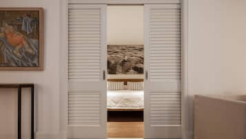 A room with a bed, a painting on the wall, and a view through a door with shutters.
