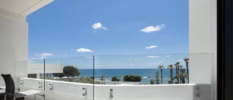 A balcony with a clear view of the sea and palm trees.