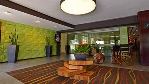 Eine Lobby mit grüner Wand mit Struktur, einem Holztisch mit einer Pflanzen-Schale und einem Streifen-Teppich.