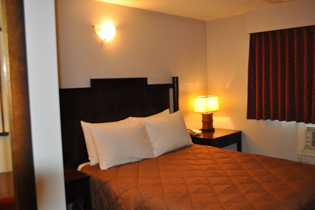Ein Hotelzimmer mit einem Bett, einem Nachttisch, einer Lampe und einem Fenster mit Vorhängen.