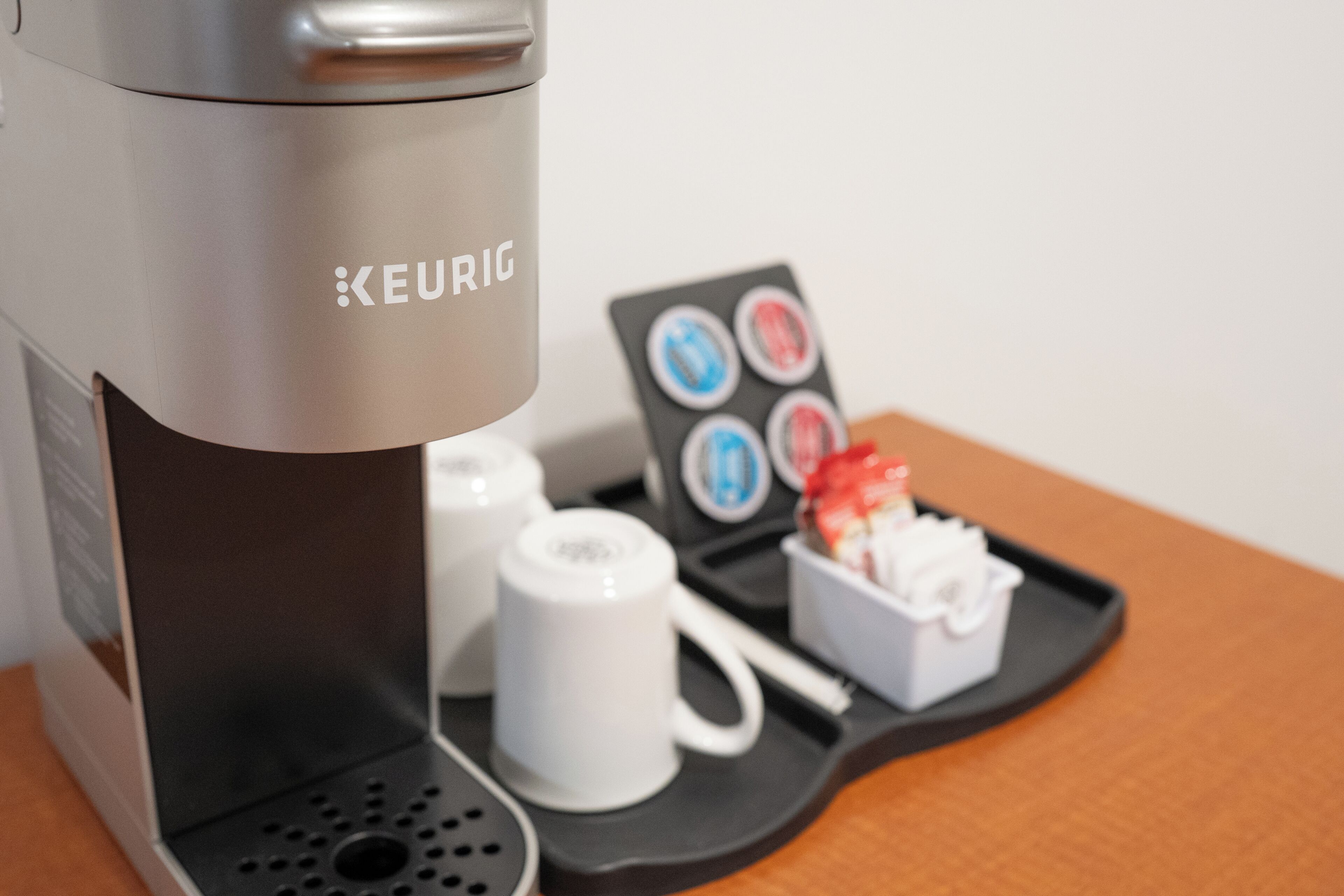 Una cafetera Keurig con un soporte para cápsulas de café y una bandeja con una taza y un pequeño recipiente.