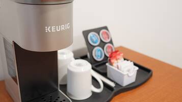 A Keurig coffee machine with a coffee pod holder and a tray with a mug and a small container.