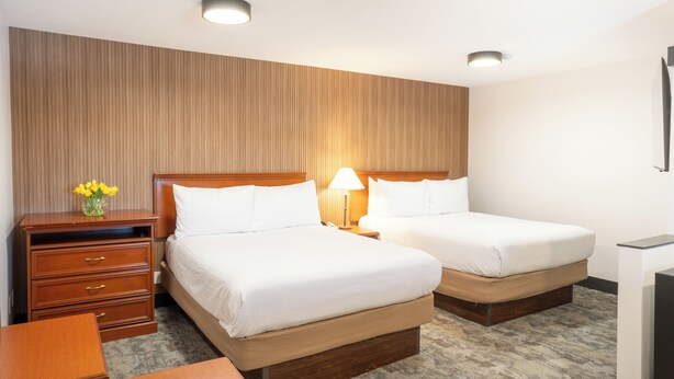 Habitación de hotel con dos camas, un aparador de madera, un escritorio y una lámpara.