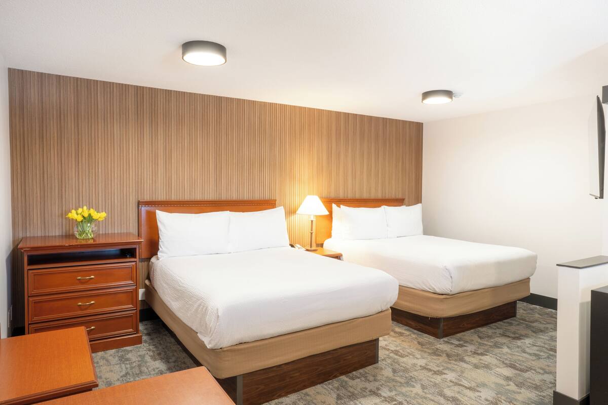 Ein Hotelzimmer mit zwei Betten, einem Holzschrank, einem Schreibtisch und einer Lampe.