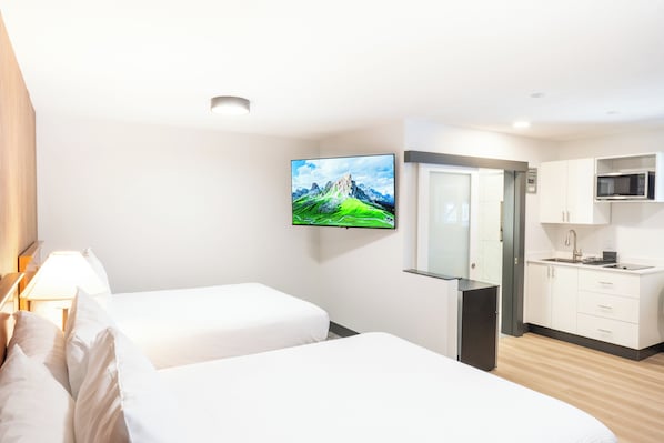 Habitación de hotel con dos camas, televisión, zona de cocina y puerta que da al baño.
