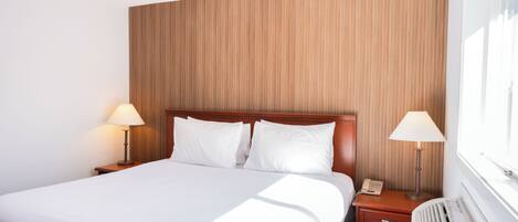 A hotel room with a large bed, two bedside tables with lamps, a heater, and a window.