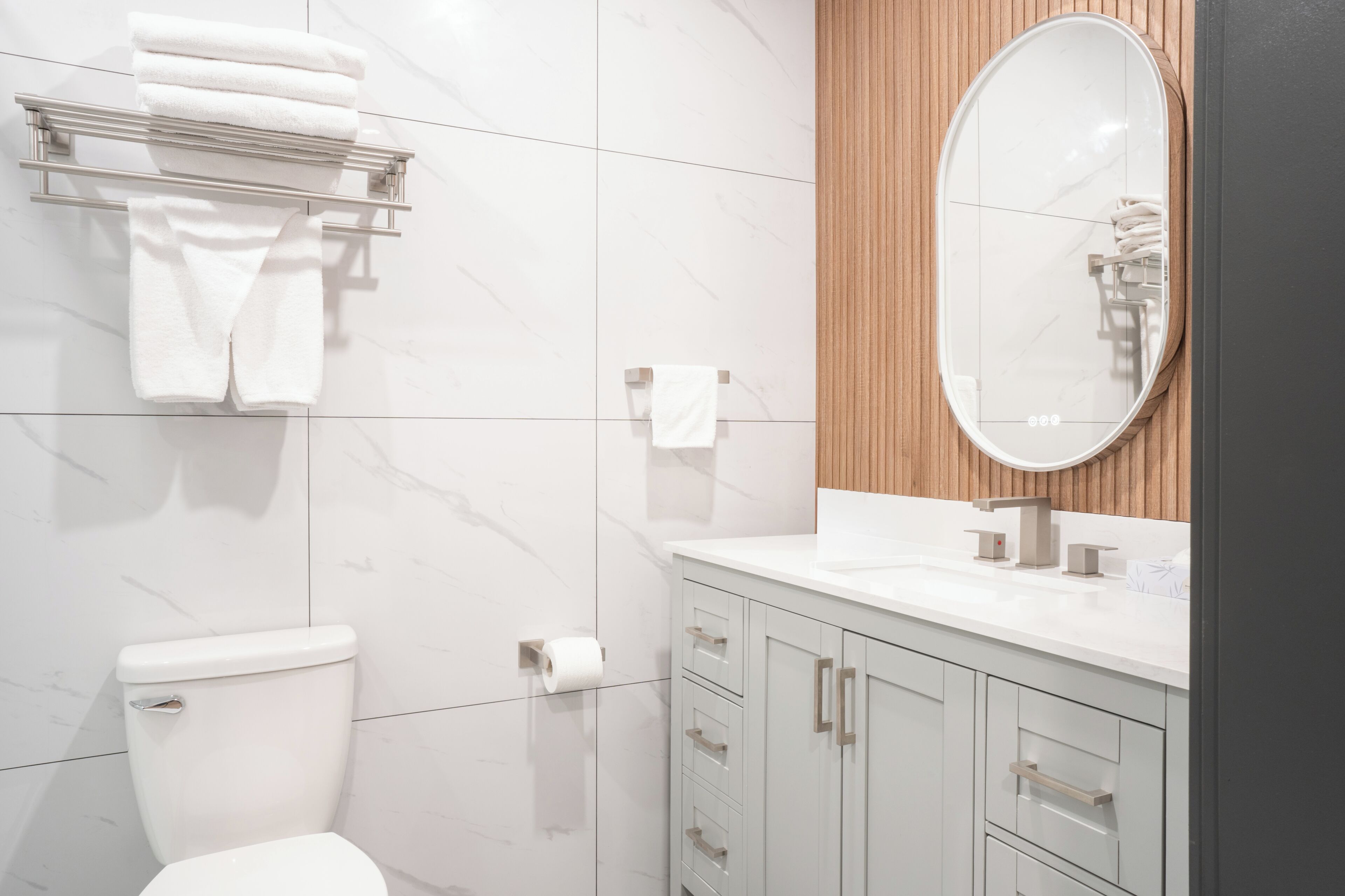Une salle de bain moderne équipée de toilettes, d’un porte-serviettes, d’un miroir et d’un meuble-lavabo avec des tiroirs.