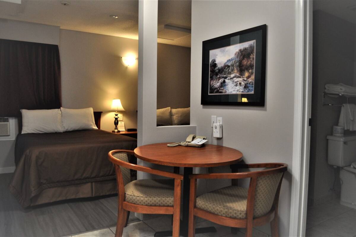 Ein Hotelzimmer mit Bett, Schreibtisch mit Stuhl, einem gerahmten Bild an der Wand und einem durchgehenden Tür sichtbaren Badezimmer.