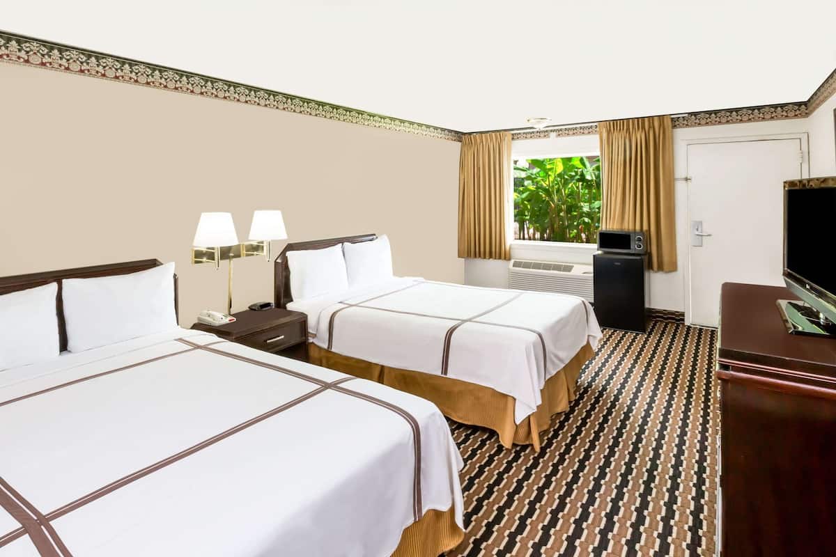 Une chambre d’hôtel avec deux lits, un bureau, une télévision et une fenêtre avec des rideaux.