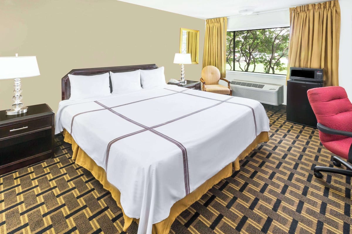 Une chambre d’hôtel avec un grand lit, un bureau, une chaise, une fenêtre avec des rideaux et un radiateur.