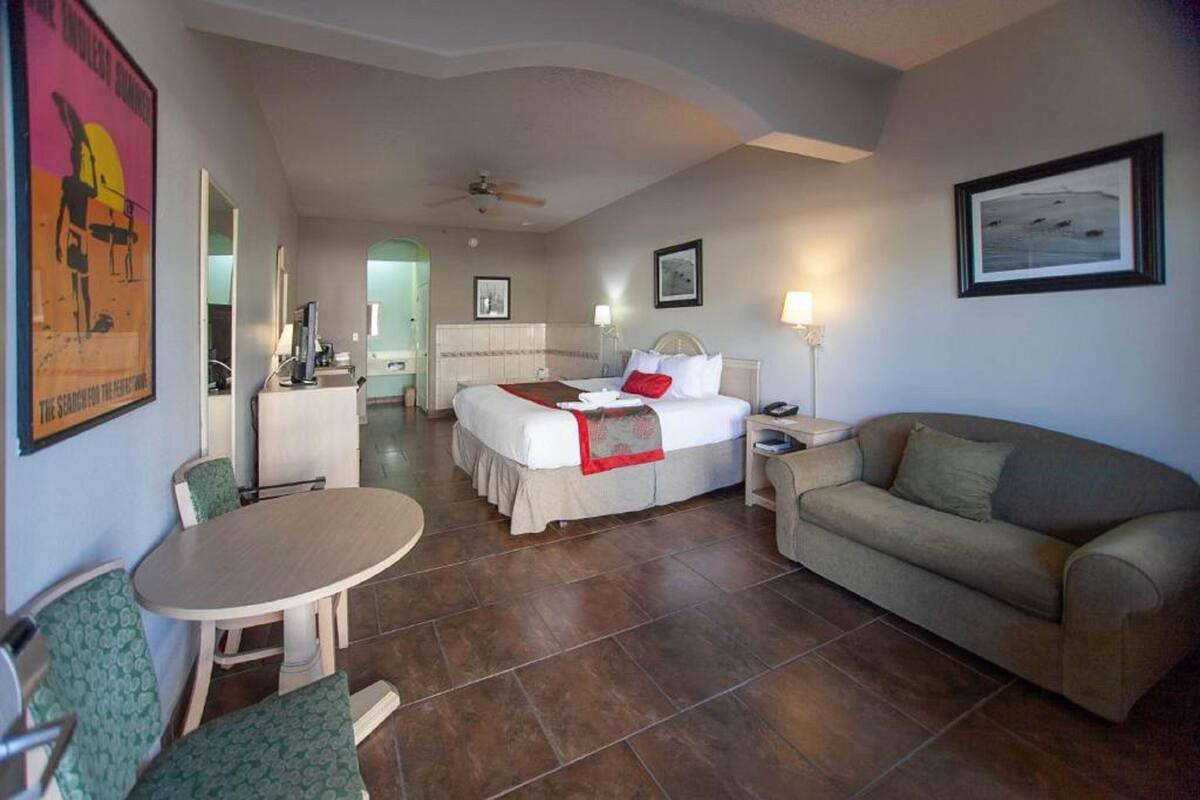 A hotel room with a bed, a sofa, a dining table, and a TV.
