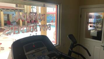 A treadmill in a room with a window overlooking a pool area.