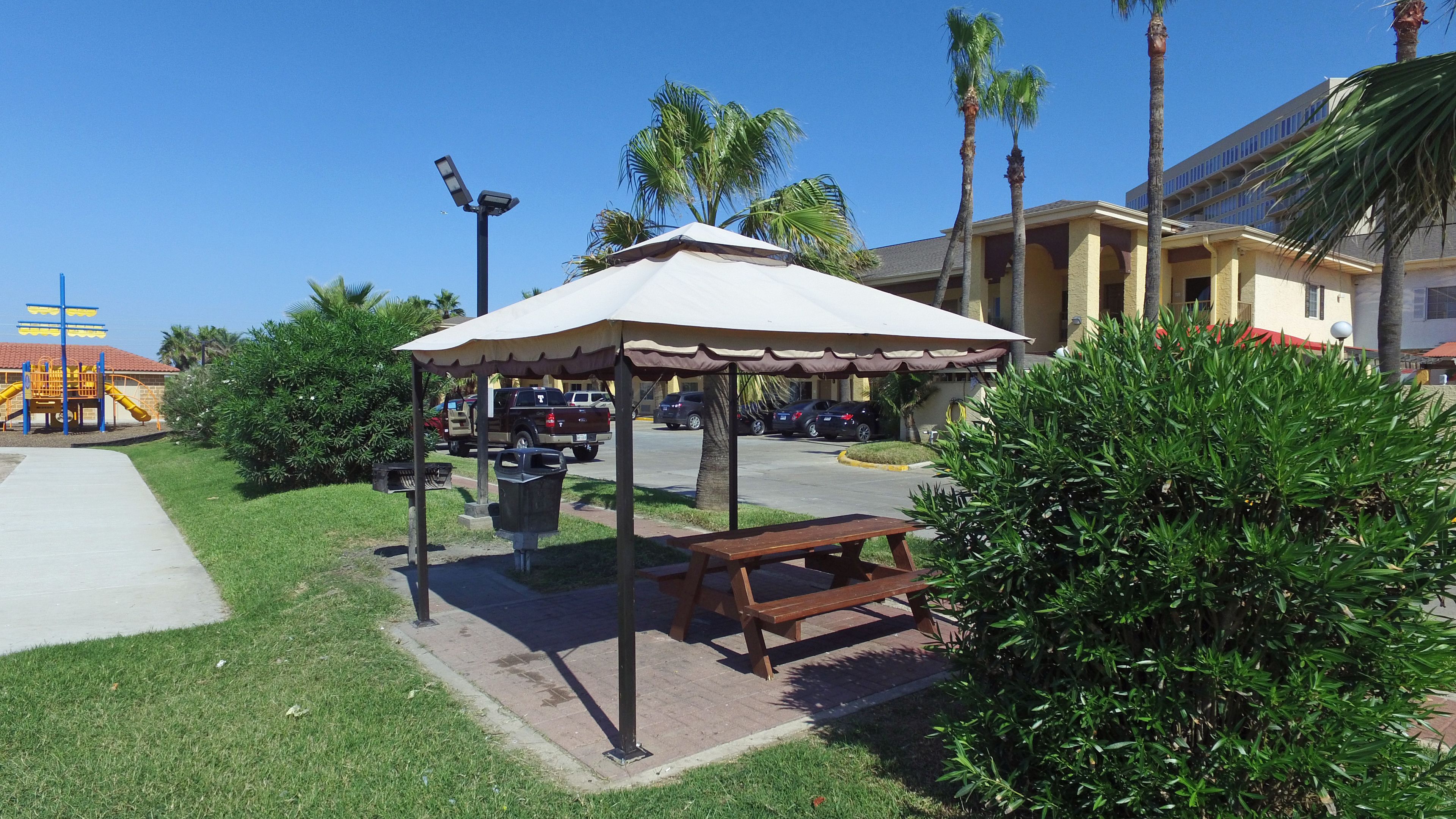 Un parc avec un kiosque, une table de pique-nique, une poubelle, une aire de jeux et des voitures garées.