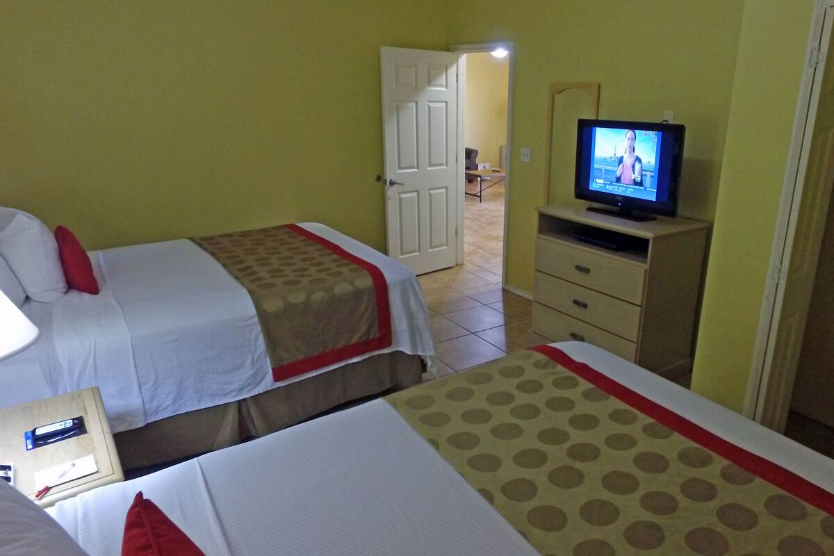 A hotel room with two beds, a television on a stand, and a door leading to another room.