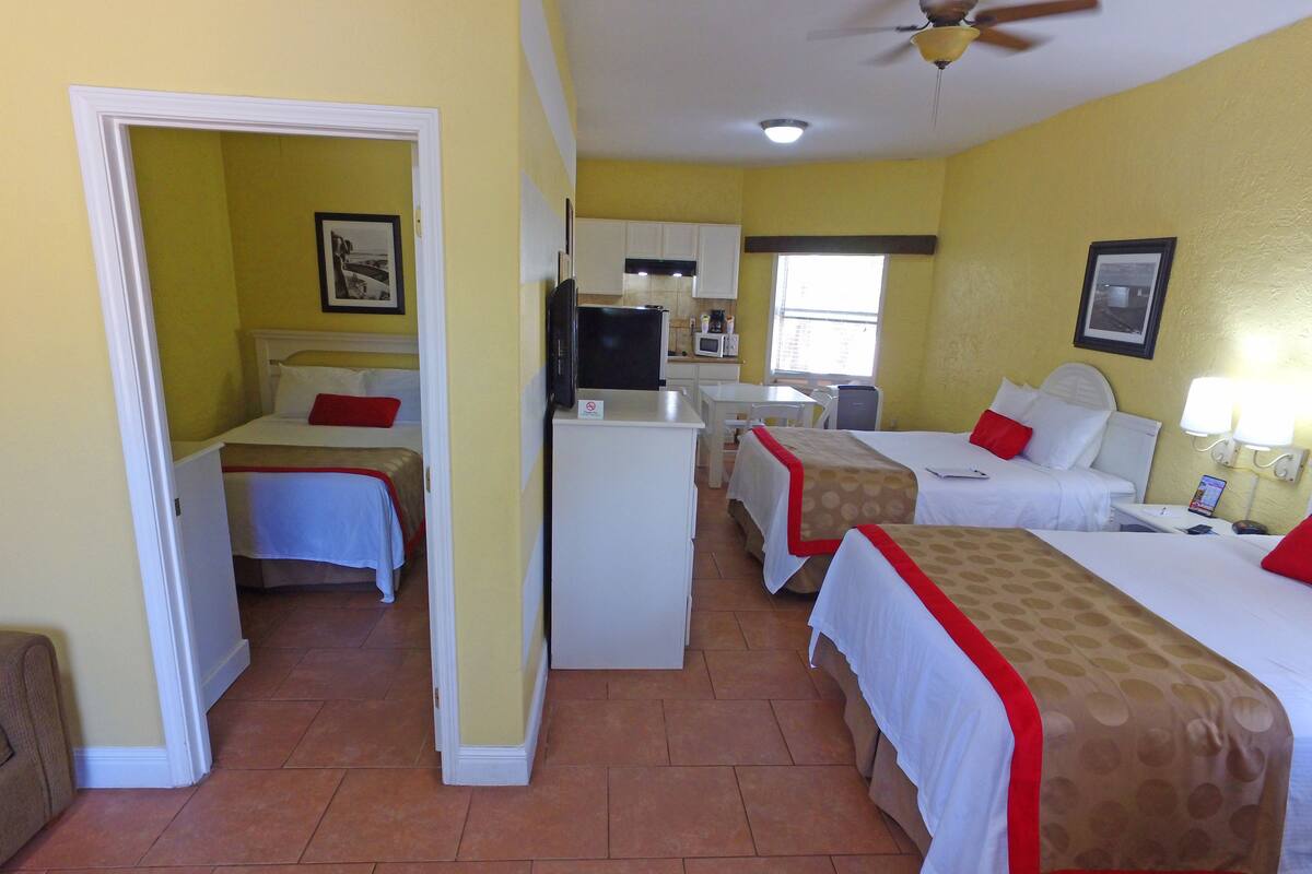 A hotel room with two beds, a kitchenette, a dining area, and a bathroom.