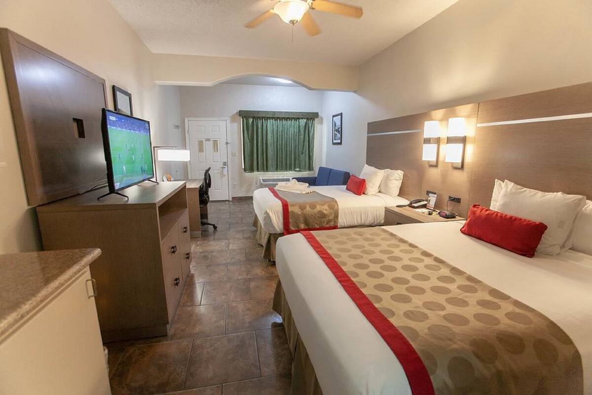 A hotel room with two beds, a desk, a television, and a bathroom.