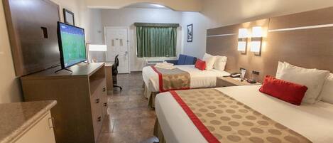 A hotel room with two beds, a desk, a television, and a bathroom.