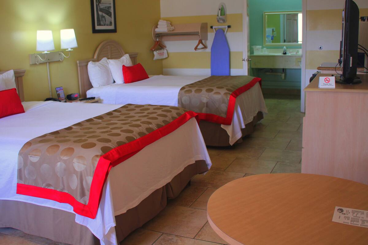 A hotel room with two beds, a desk, a chair, a bathroom visible through an open door, and a TV on a stand.