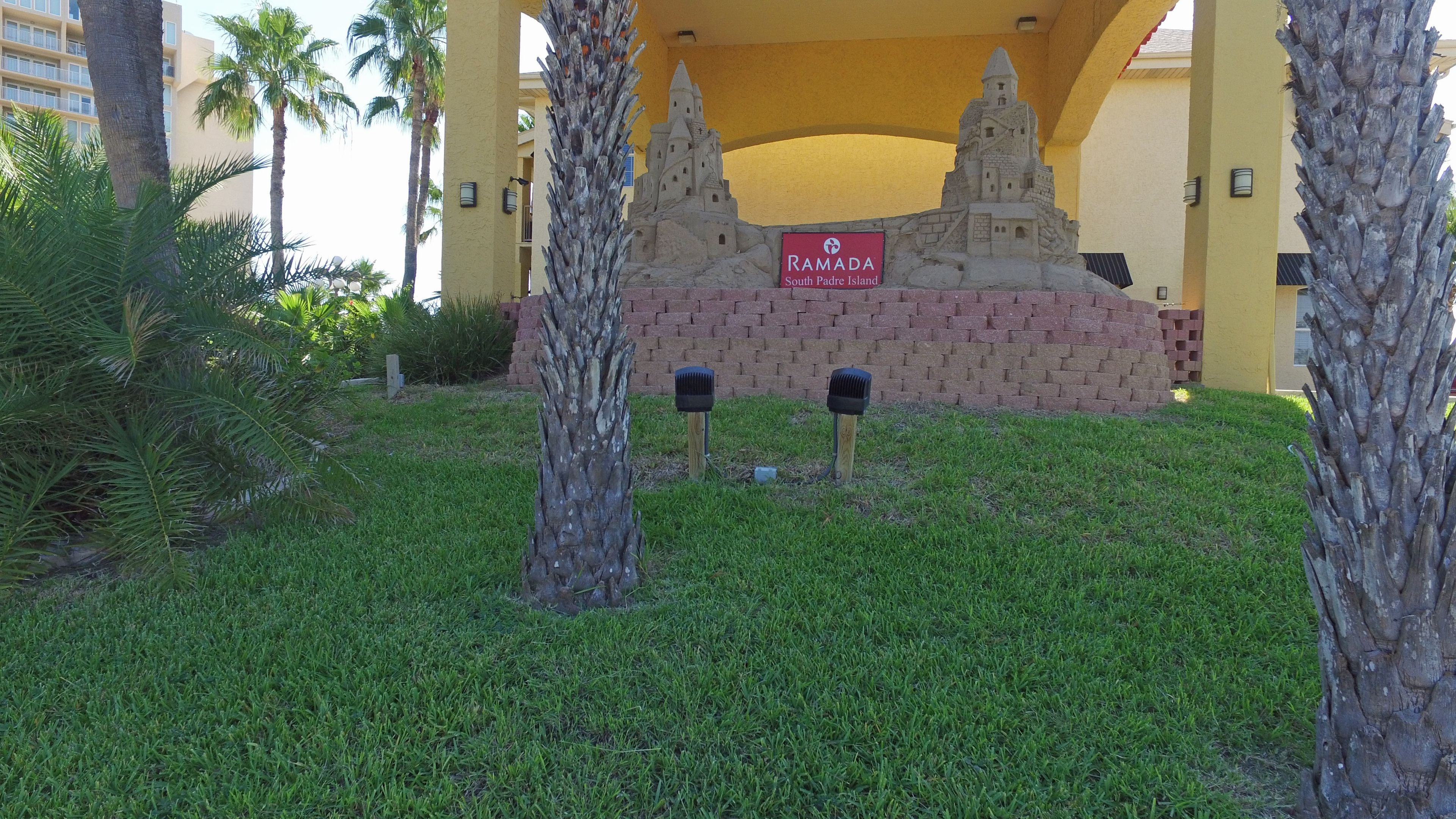Une enseigne indiquant « Ramada South Padre Island », avec un mur de briques et des palmiers au premier plan.